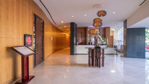 A modern hotel lobby with a reception desk, a digital information board, and a seating area with a vase of flowers. - Miyako Hybrid Hotel Torrance (Torrance)