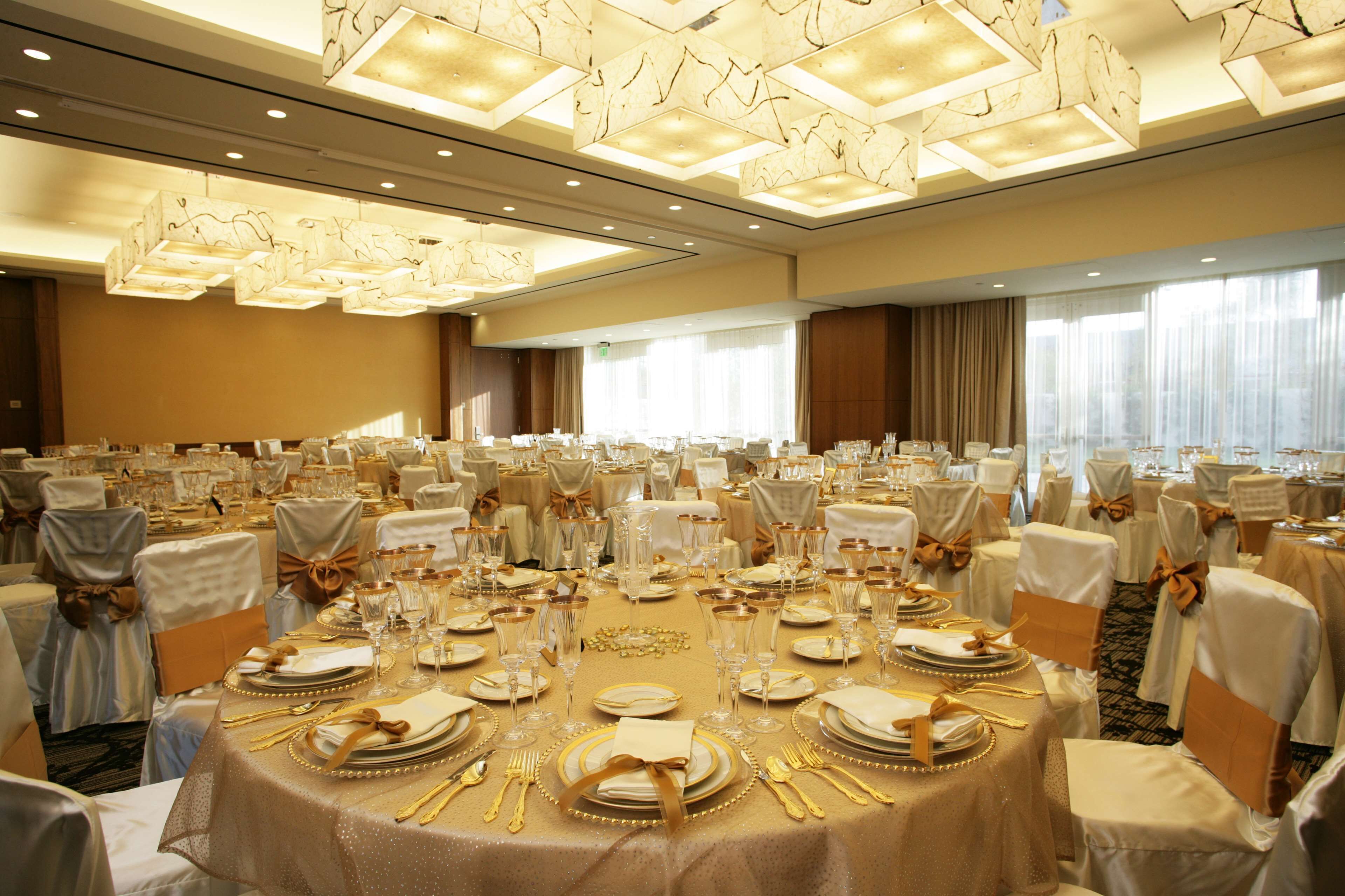 A banquet hall with round tables set for a formal event, featuring gold accents and white chairs with gold sashes.
