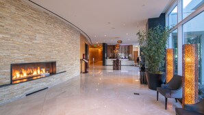 A modern lobby with a stone wall, a fireplace, seating area, and large windows. - Miyako Hybrid Hotel Torrance (Torrance)