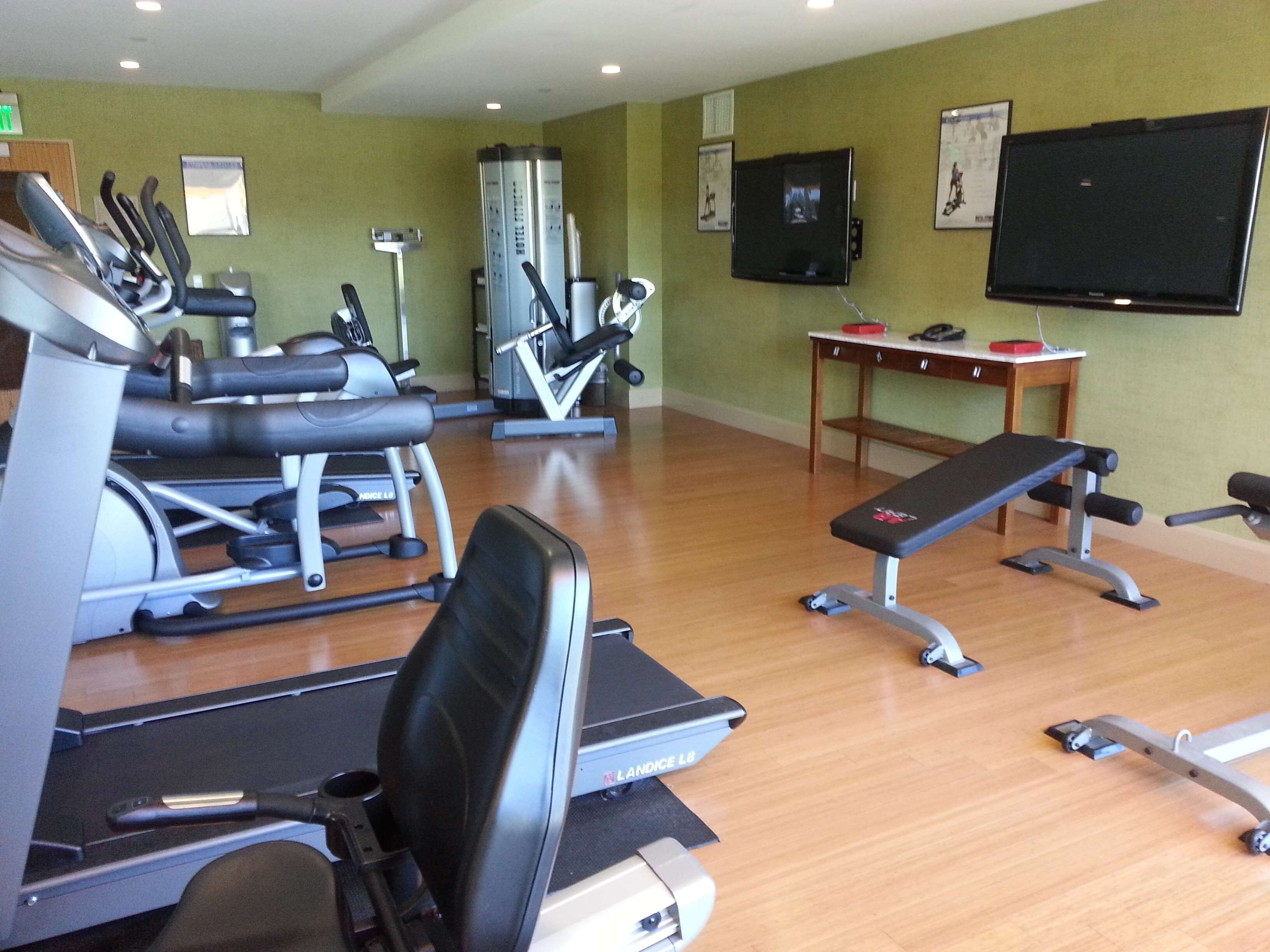Een sportschool met diverse fitnessapparaten, een bank en een televisie aan de muur.