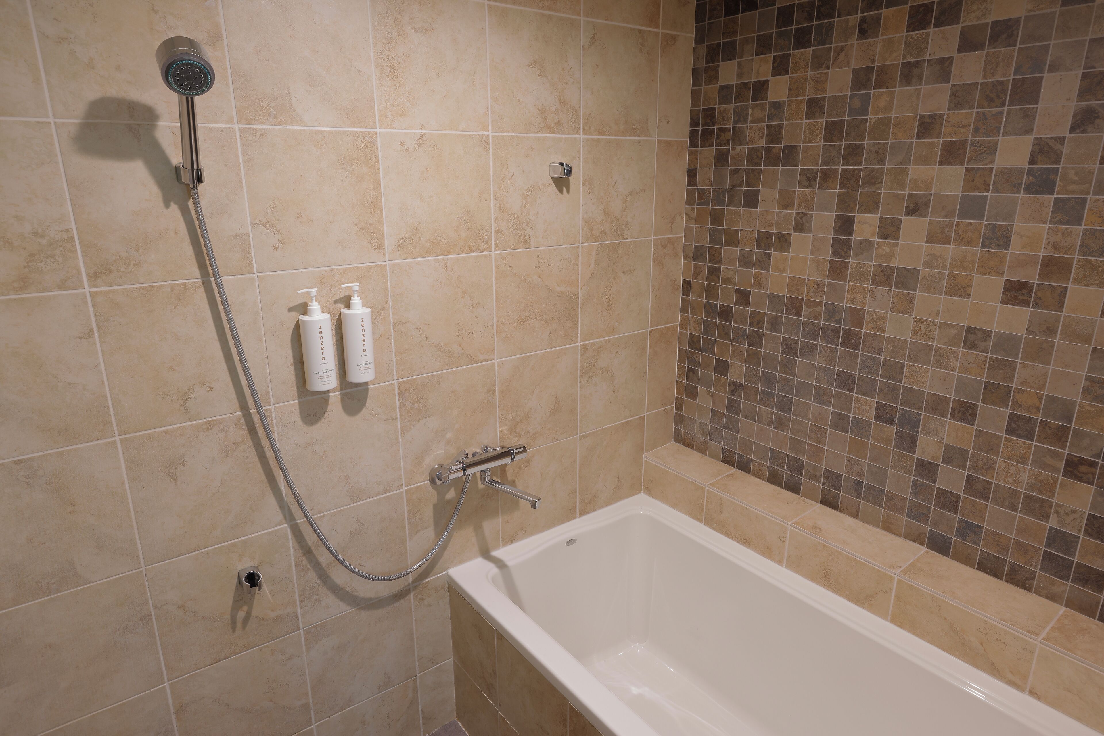 A bathroom with a bathtub, a showerhead, and two bottles of shampoo.