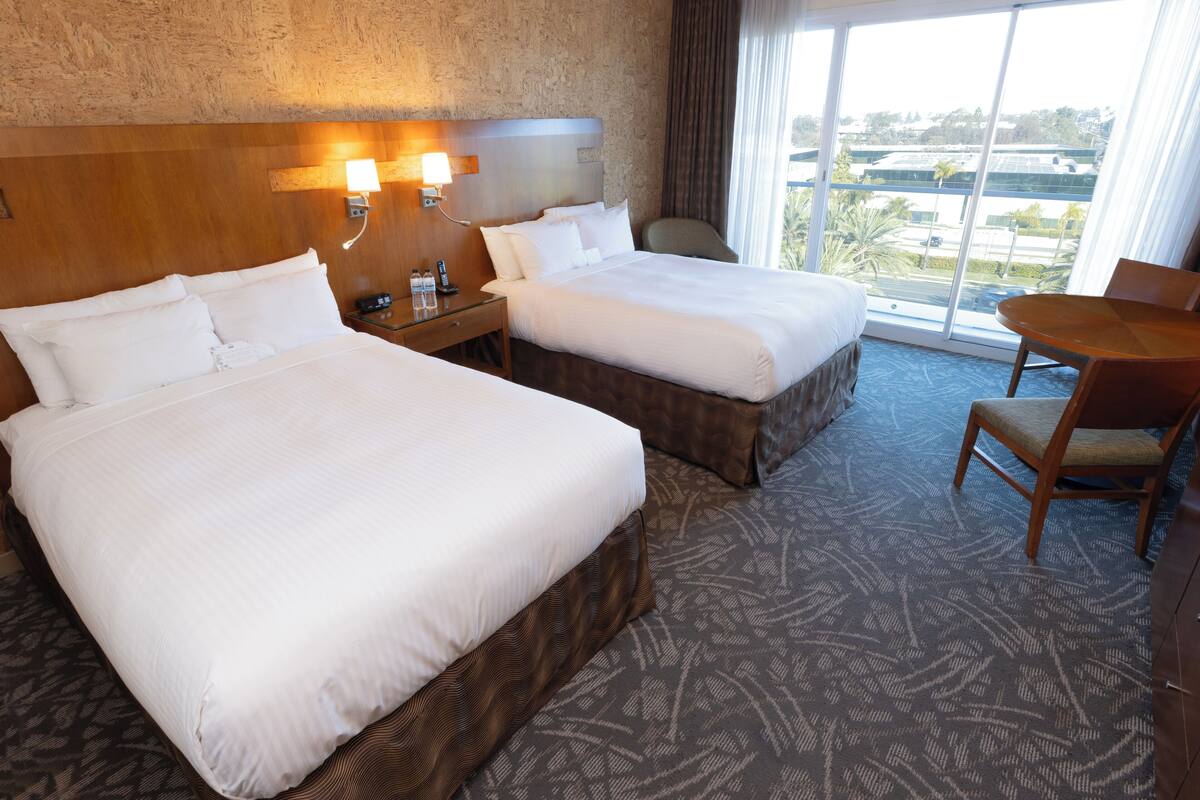 A hotel room with two beds, a desk, and a chair.