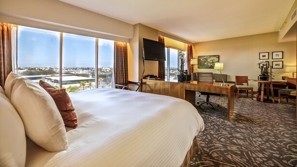 A hotel room with a large bed, a desk with a computer, and a view of the city. - Miyako Hybrid Hotel Torrance (Torrance)