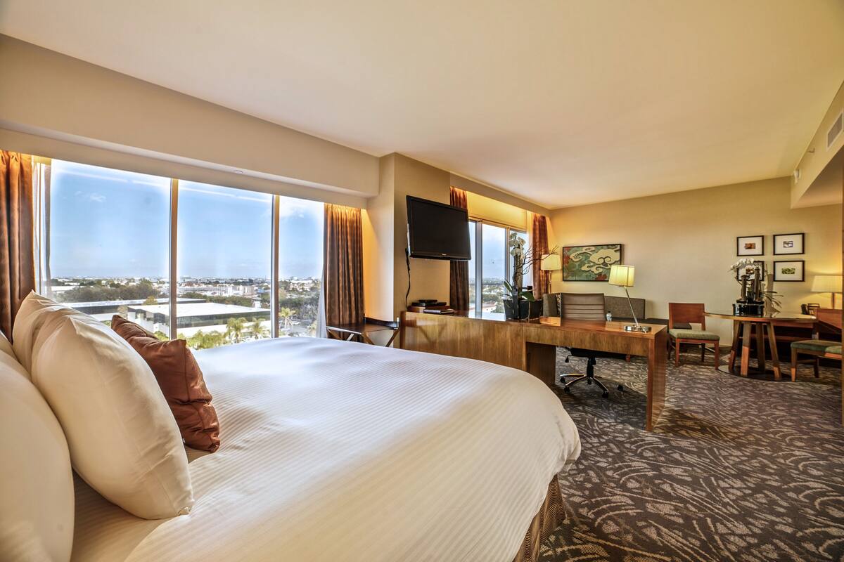 A hotel room with a large bed, a desk with a computer, and a view of the city.