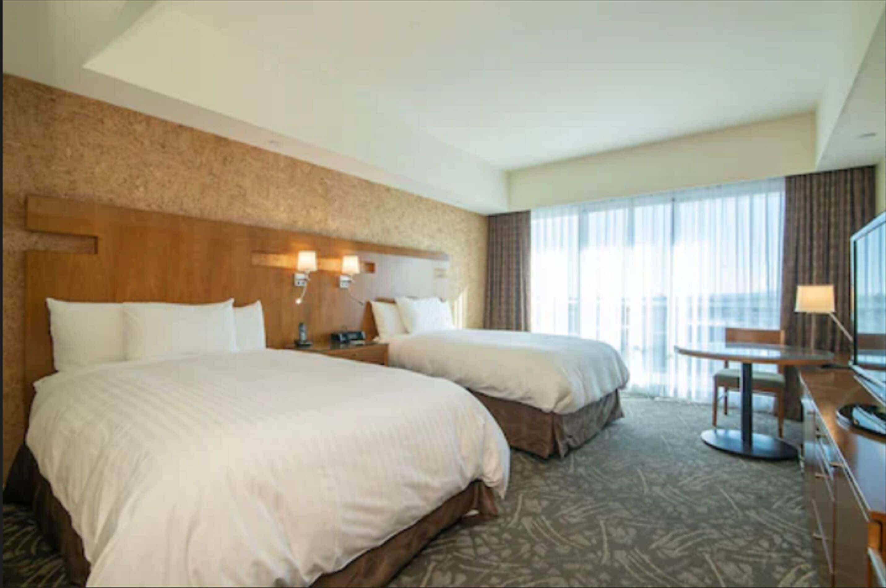 A hotel room with two beds, a desk, and a TV.