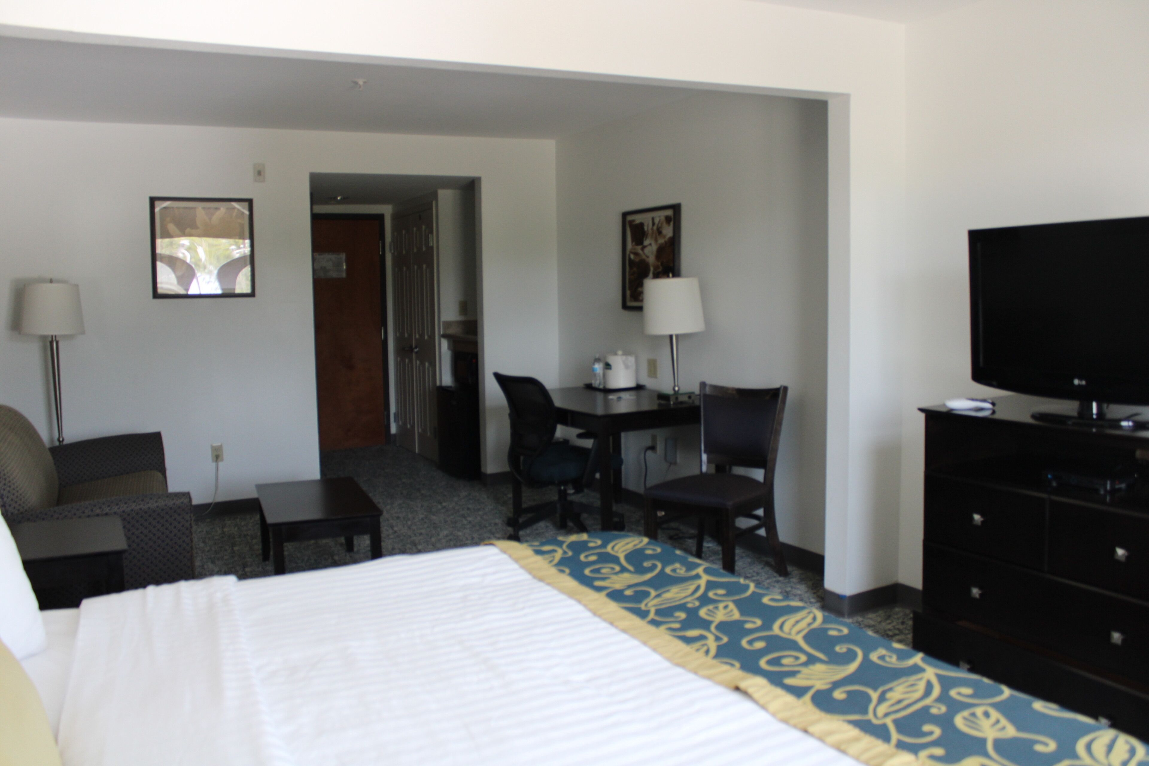 A hotel room with a bed, a desk, a chair, a television, and a lamp.