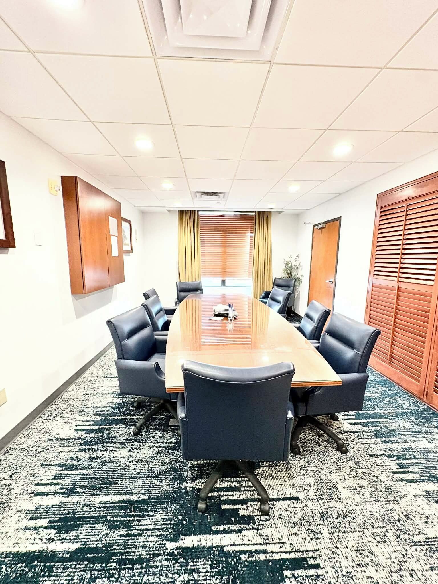 Una sala de conferencias con una larga mesa, sillas negras, alfombra estampada y paneles de madera en las paredes.