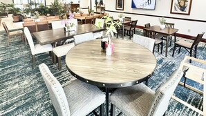 A spacious hotel lobby with multiple dining areas, including a central round table with chairs, surrounded by sofas and additional tables. - Wingate by Wyndham Houma LA (Houma)