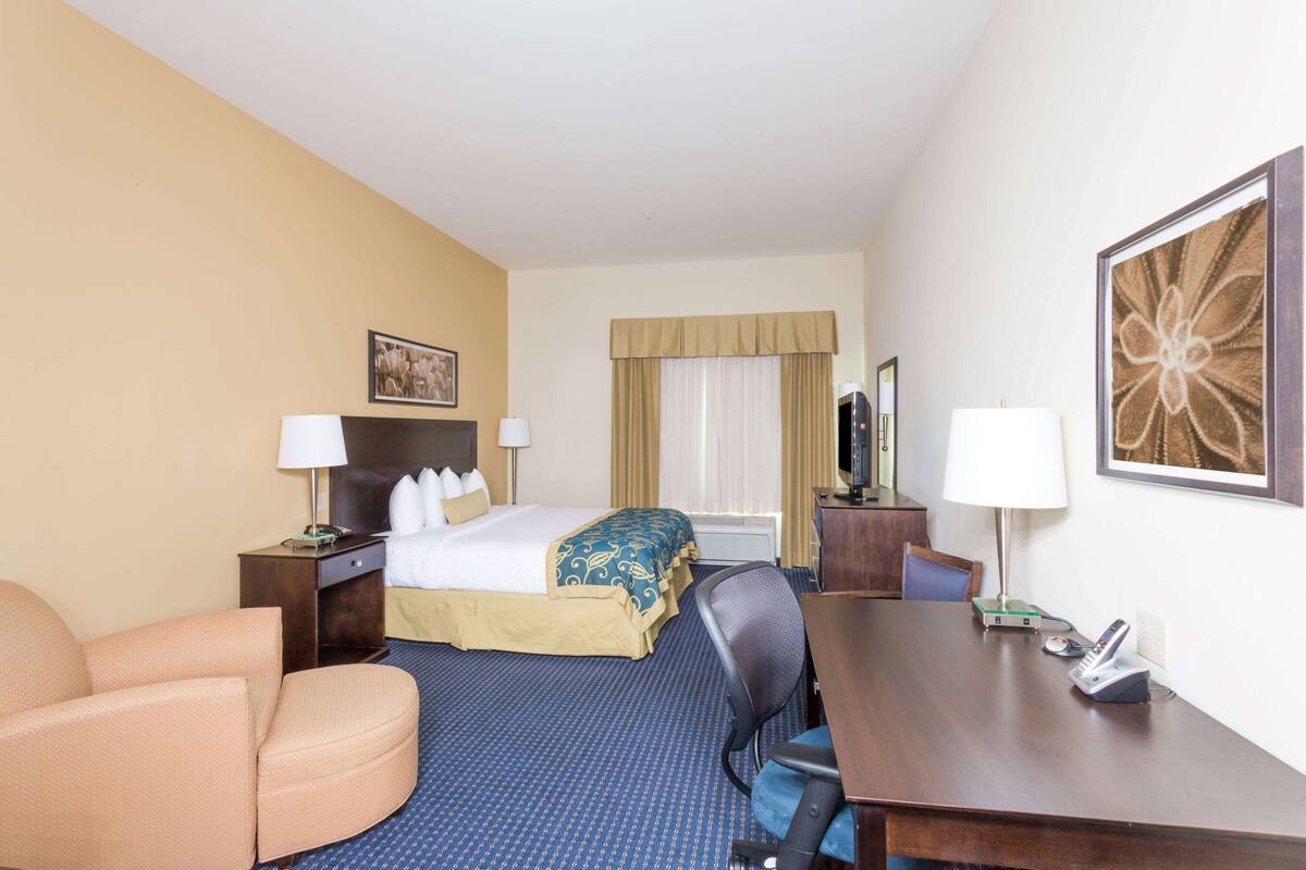 A hotel room with a bed, a desk, a chair, a lamp, and a painting on the wall.
