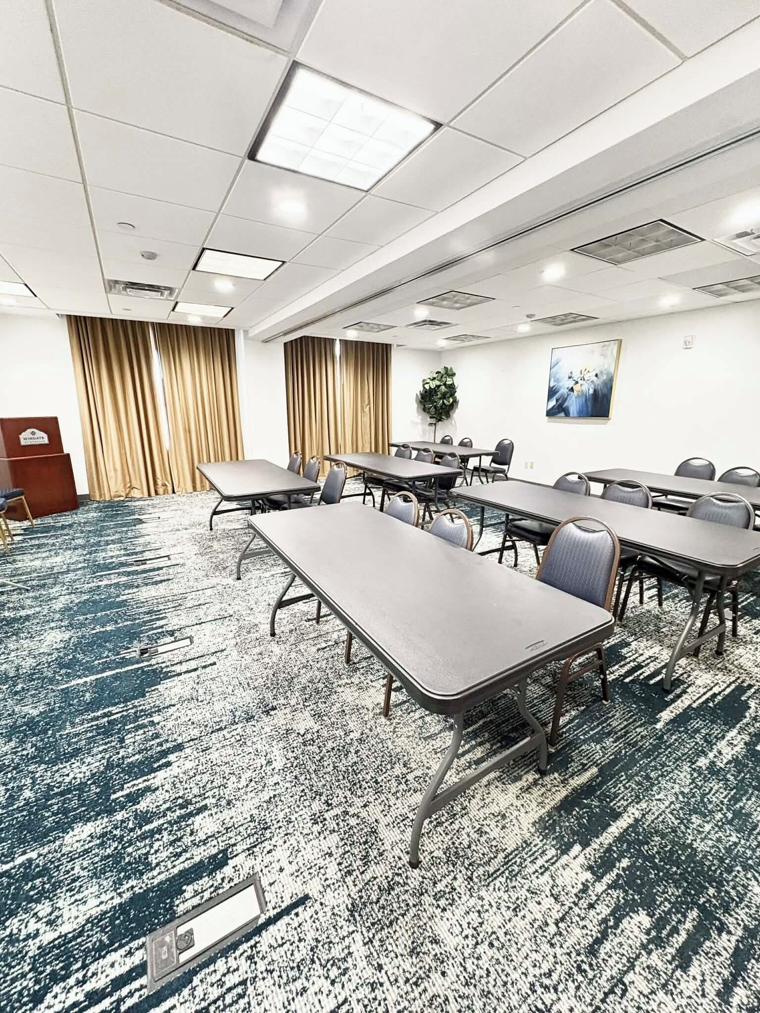 A conference room with multiple tables and chairs, a podium, and a large window with curtains.