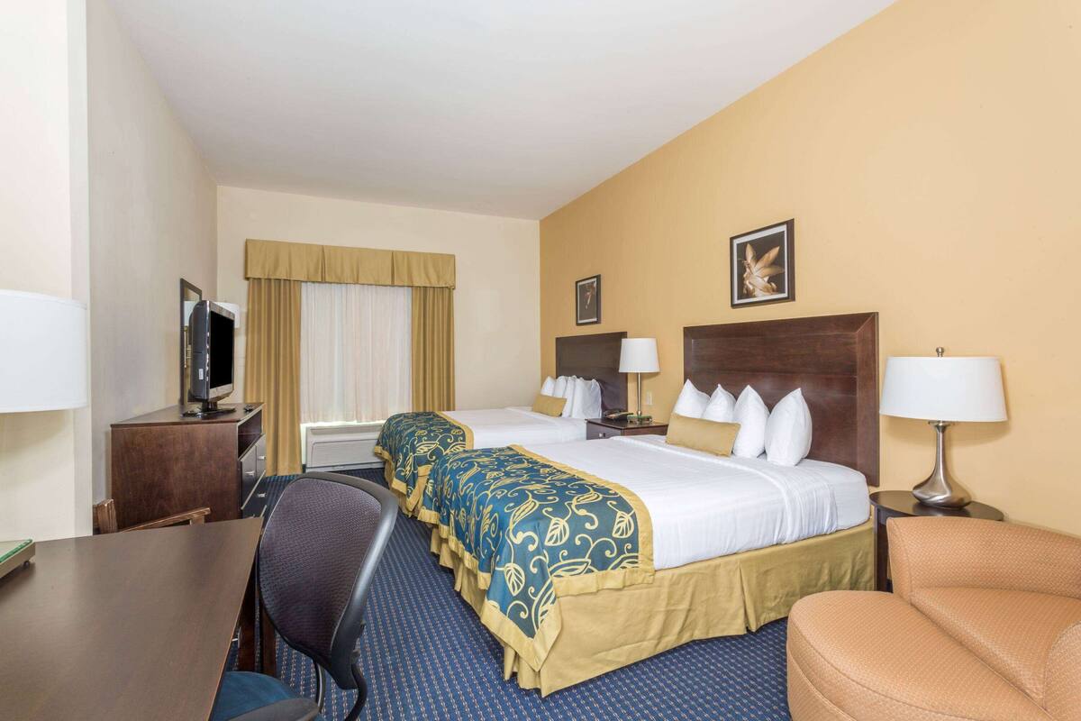 A hotel room with two beds, a desk, a chair, and a television.