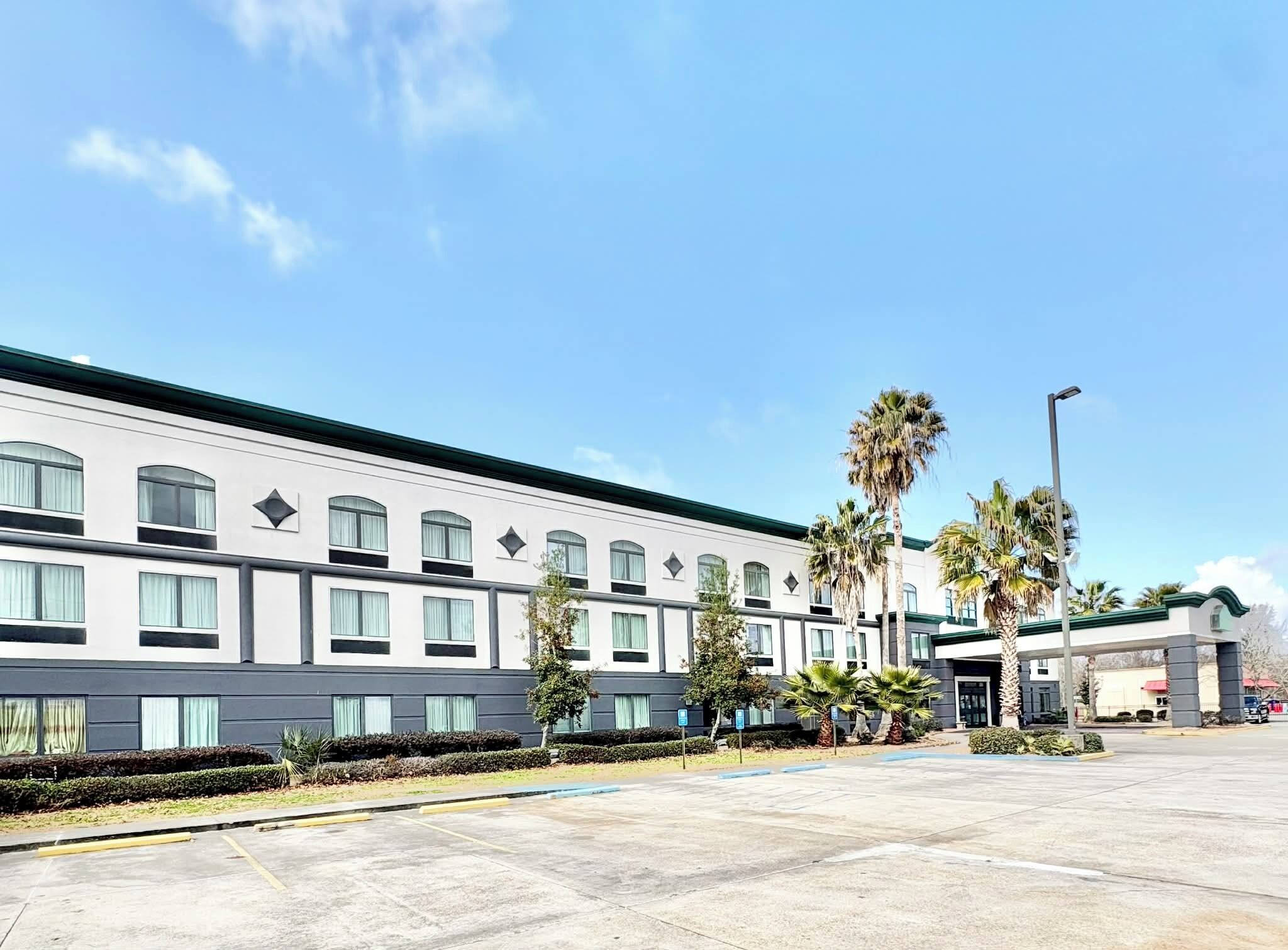 A modern hotel with a flat facade, multiple windows, and a parking lot with palm trees.