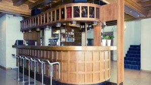Un espace bar doté d’un comptoir en bois incurvé, de tabourets de bar et d’une bibliothèque contenant divers objets.