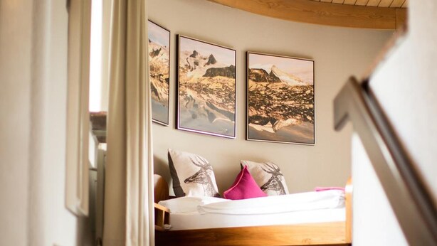 Un escalier menant à une chambre à coucher, avec un lit, un plafond en bois et des tableaux encadrés accrochés au mur.