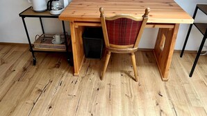 Une table de salle à manger en bois, accompagnée d’une chaise, d’une machine à café et d’un panier, le tout posé sur un support en métal noir.