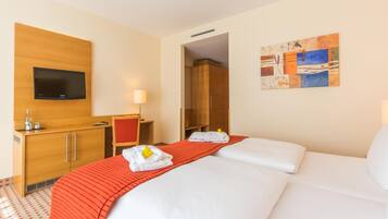 Una habitación de hotel con cama, escritorio, televisor, un cuadro y alfombra roja.
