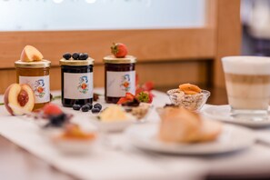 Una mesa de desayuno con diversas opciones de comida, incluyendo frutas, pasteles y frascos de conservas.