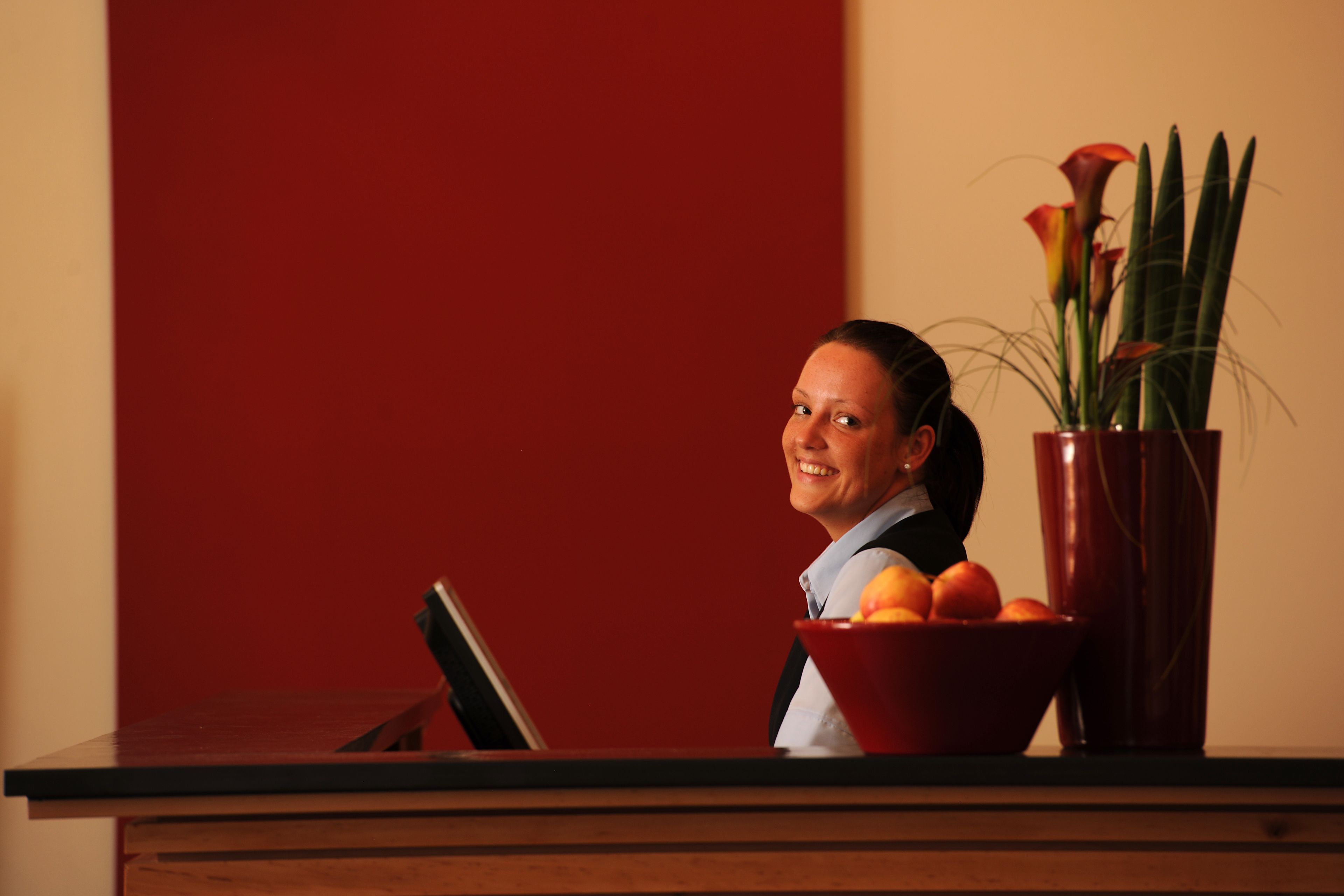 Ein Empfangstresen mit roter Wand, einer Vase mit Blumen und einer Schale Orangen.