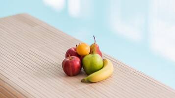 Una mesa de madera con una composición de frutas junto a una piscina.