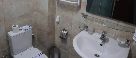 Baño con inodoro, lavamanos y cabina de ducha de vidrio.
