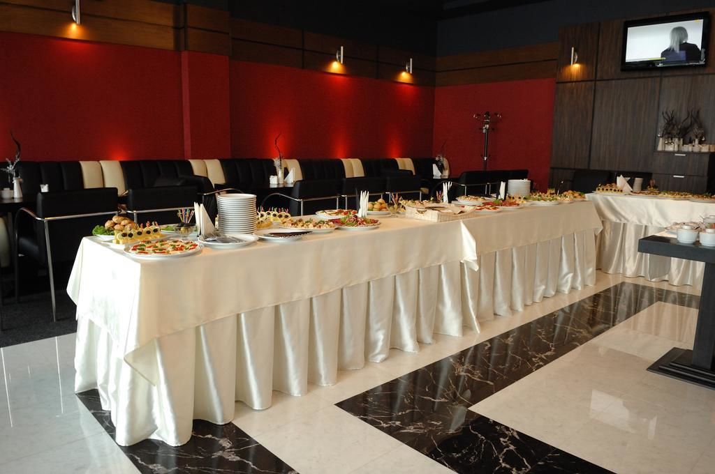 Un salón de conferencias con una larga mesa dispuesta para un bufé, sillas de cuero negro, una pantalla de televisión y una pared roja de acento.