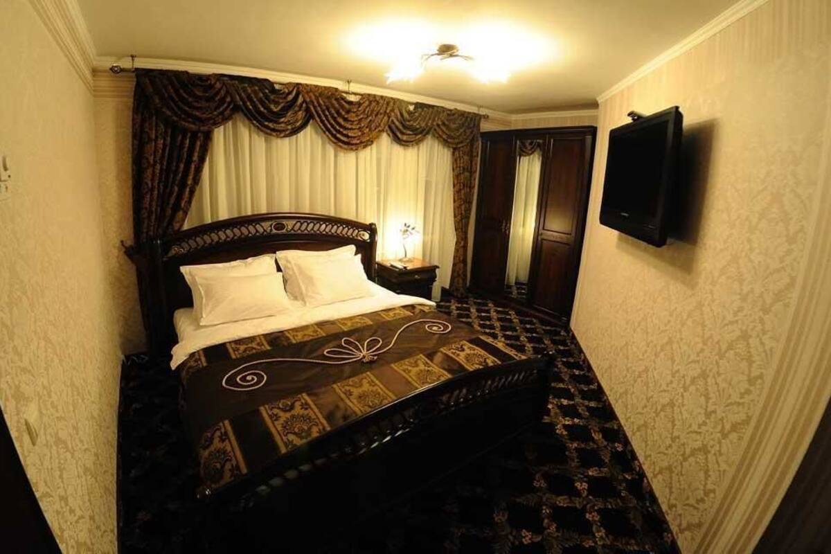 A bedroom with a large bed, a television mounted on the wall, and a patterned carpet.
