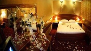 A hotel room with a bed, a bedside table with a vase of flowers, and a wall-mounted light fixture. - Mir Hotel In Rovno (Rivne)