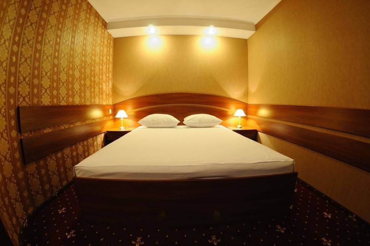 A hotel room with a large bed, two bedside lamps, and a patterned wallpaper.