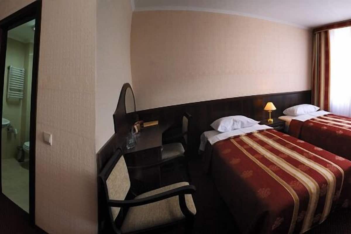 A hotel room with two beds, a desk, a chair, a television, and a bathroom visible through an open door.