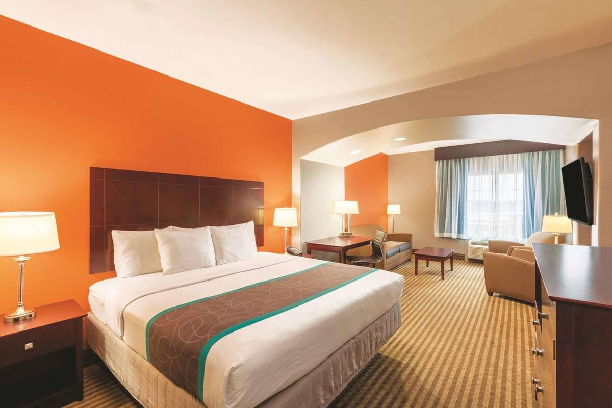 A hotel room with a large bed, two bedside tables, a desk, a chair, a TV, and a window with curtains.