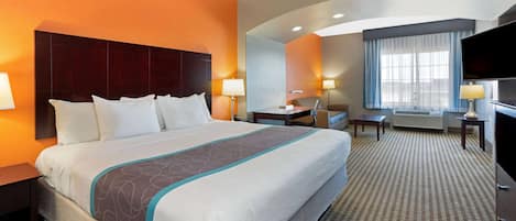 A hotel room with a large bed, a desk, a chair, a television, and a window with curtains.