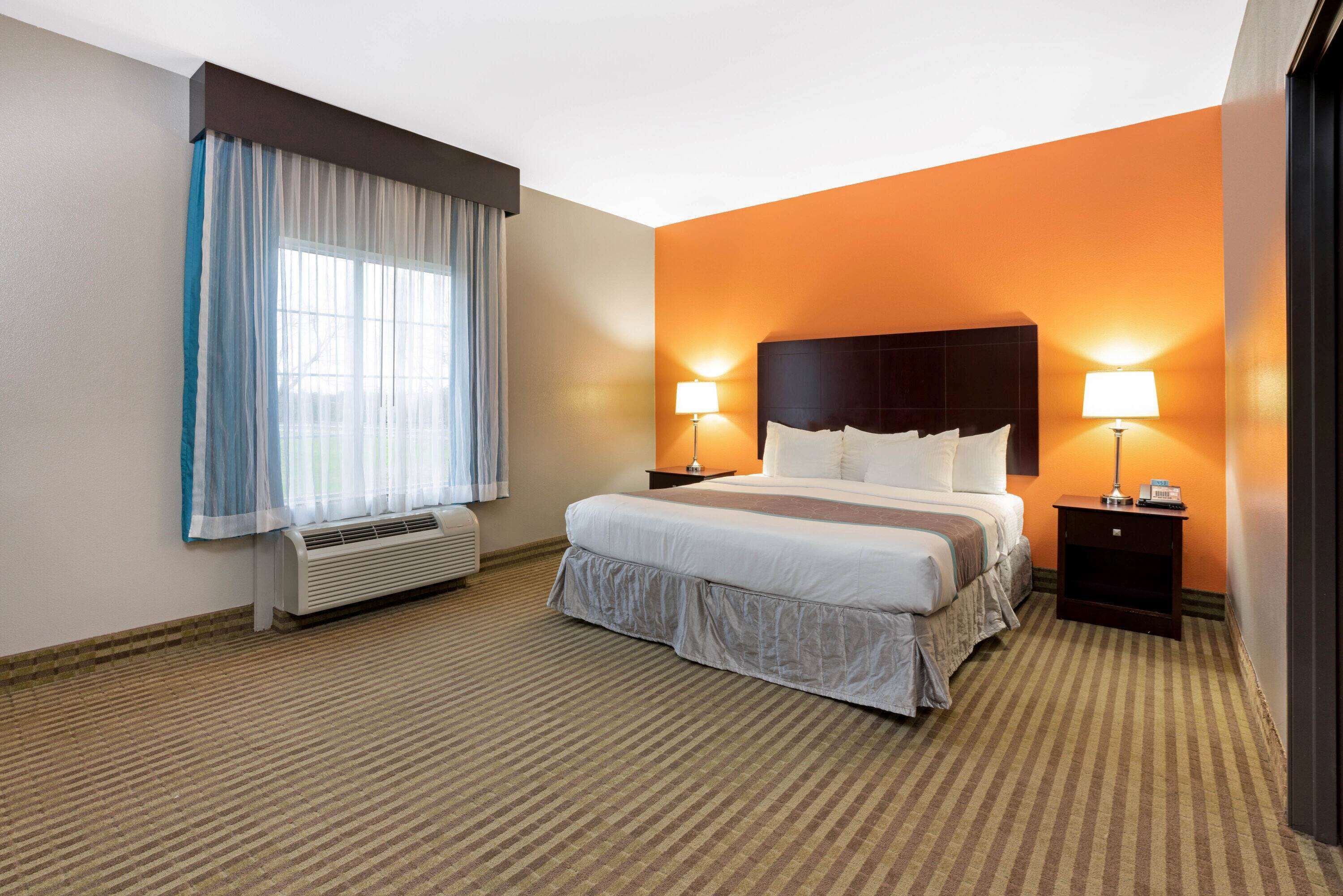 Una habitación de hotel con una cama grande, dos mesitas de noche con lámparas, una ventana con cortinas y un equipo de aire acondicionado.