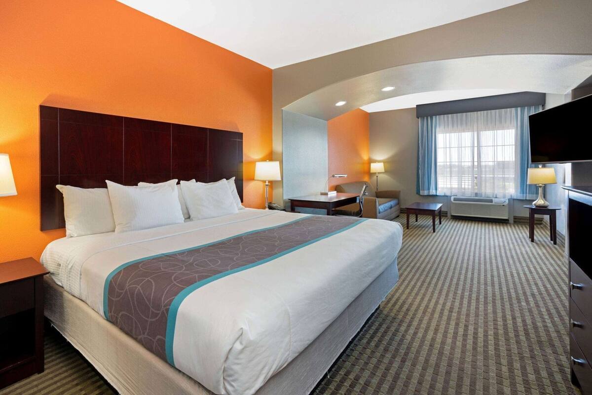 A hotel room with a large bed, a desk, a chair, a TV, and a window with curtains.