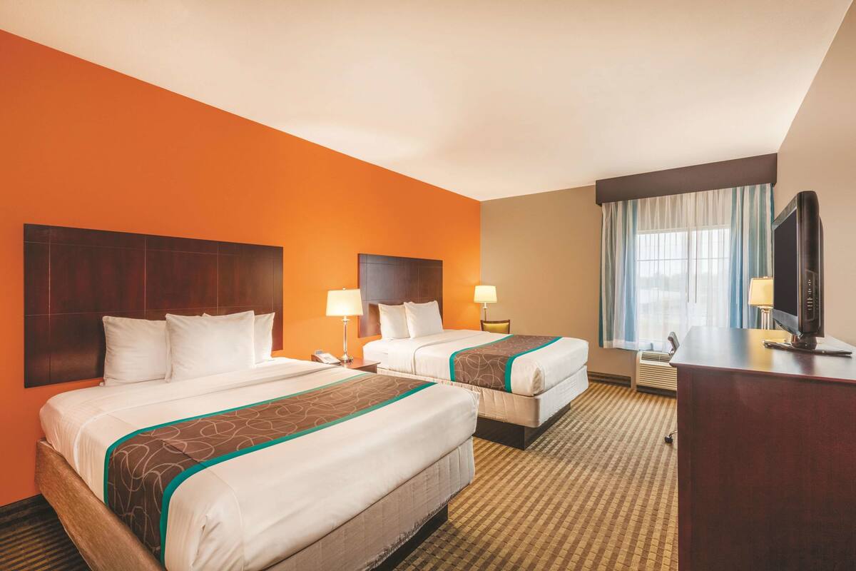 A hotel room with two beds, a desk, a TV, and a window with curtains.