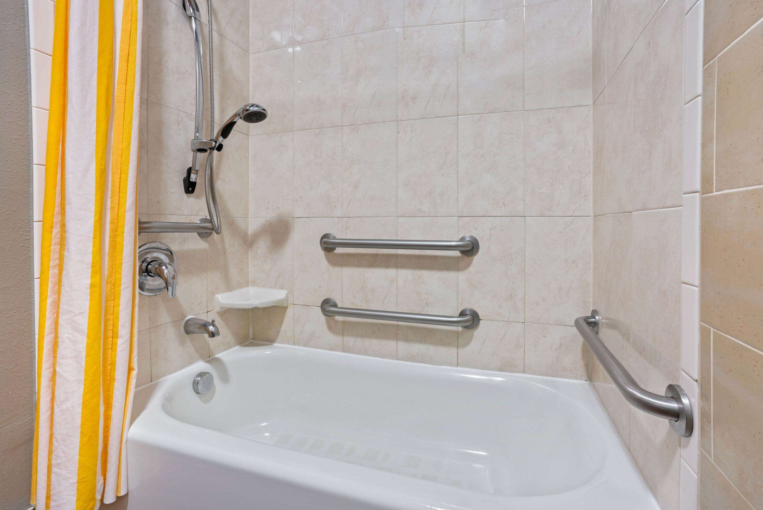 A bathroom with a bathtub, grab bars, and a shower head.