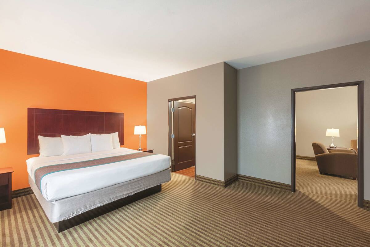 A hotel room with a large bed, a wooden headboard, two bedside tables with lamps, a door, and a mirror.
