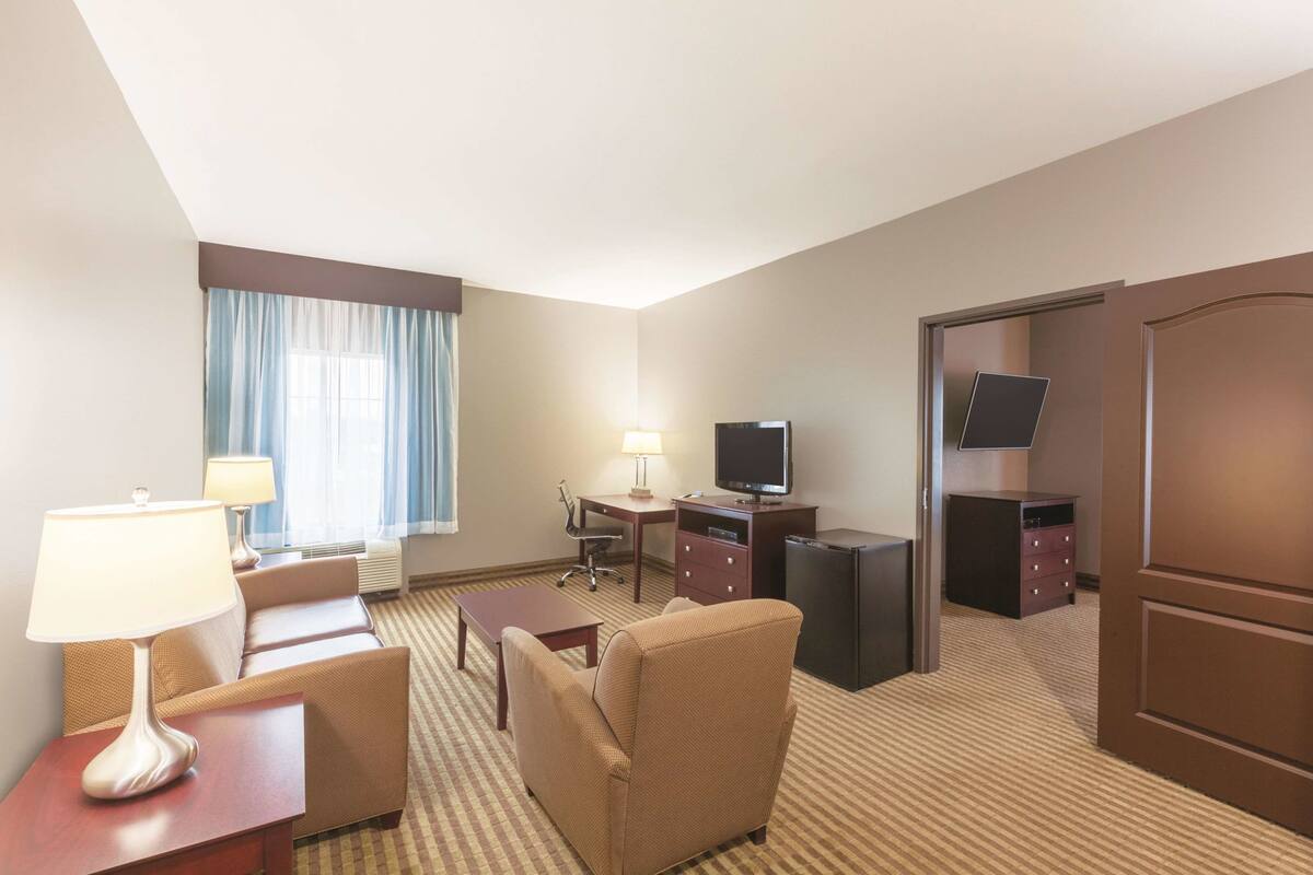 A hotel room with a sofa, two lamps, a desk with a TV, a dresser, and a door.