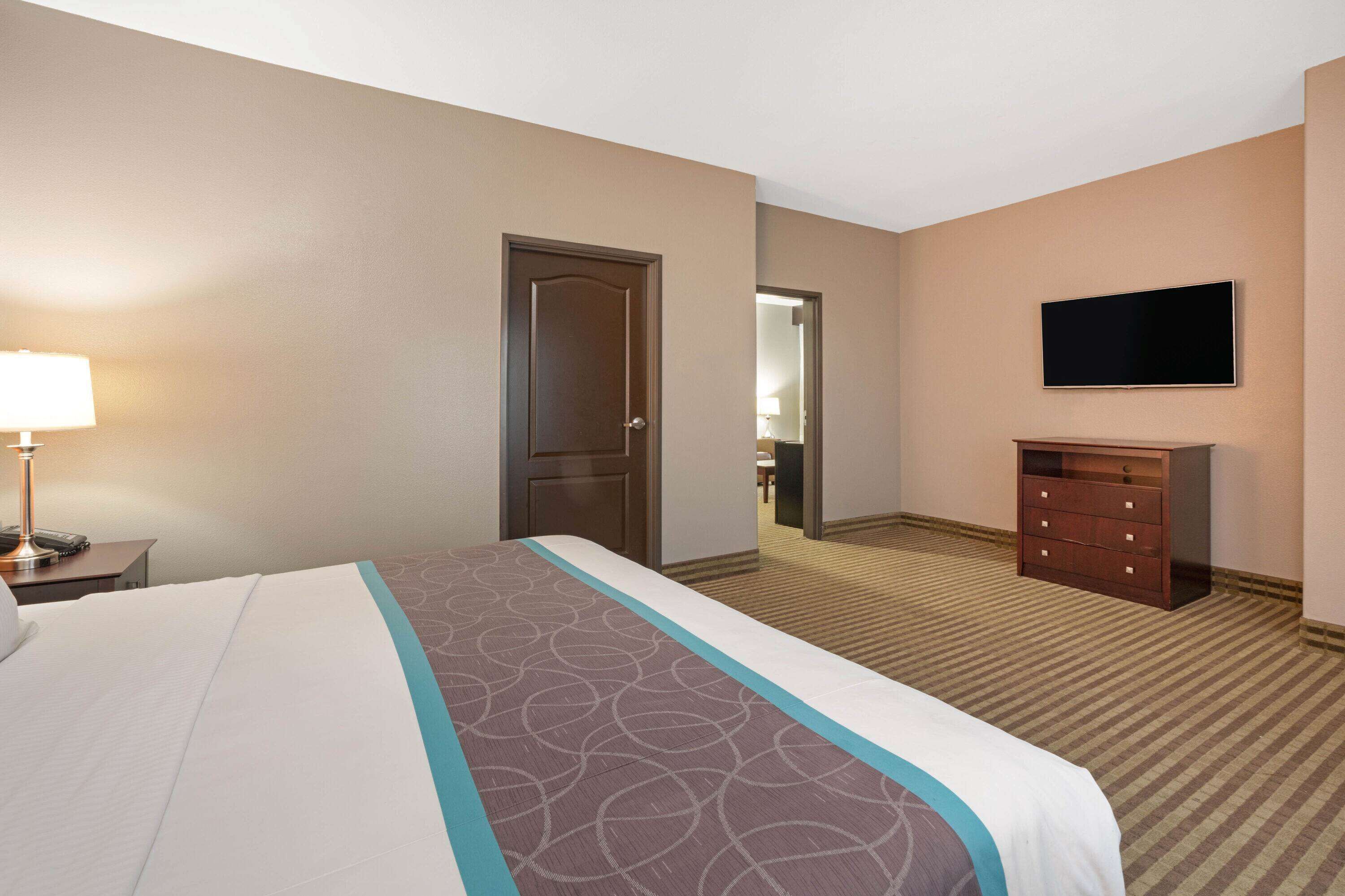 A hotel room with a bed, a dresser, a television, and a door leading to another room.