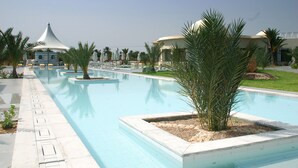 A swimming pool with palm trees and umbrellas, surrounded by buildings with a modern design. - Cesar Thalasso (Djerba Midun)