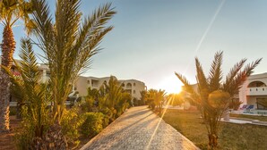A paved pathway leading to a building with multiple balconies, surrounded by palm trees and a clear sky. - Cesar Thalasso (Djerba Midun)