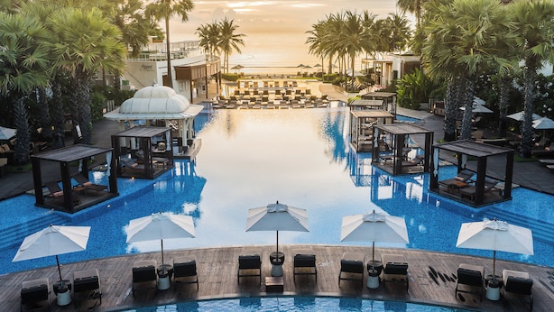 A resort pool with lounge chairs and umbrellas, surrounded by palm trees and a view of the ocean. - Intercontinental Hua Hin Resort by IHG (Hua Hin)