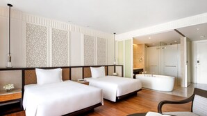 A hotel room with two beds, a large bathtub, a wooden floor, and a modern design.
