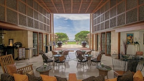 Un espacio interior con mesas y sillas, vista a un jardín y un techo decorativo.