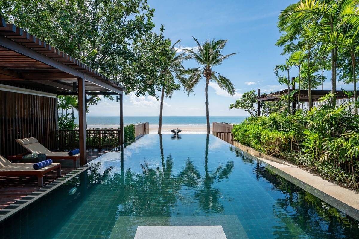 A swimming pool with lounge chairs and a view of the beach.