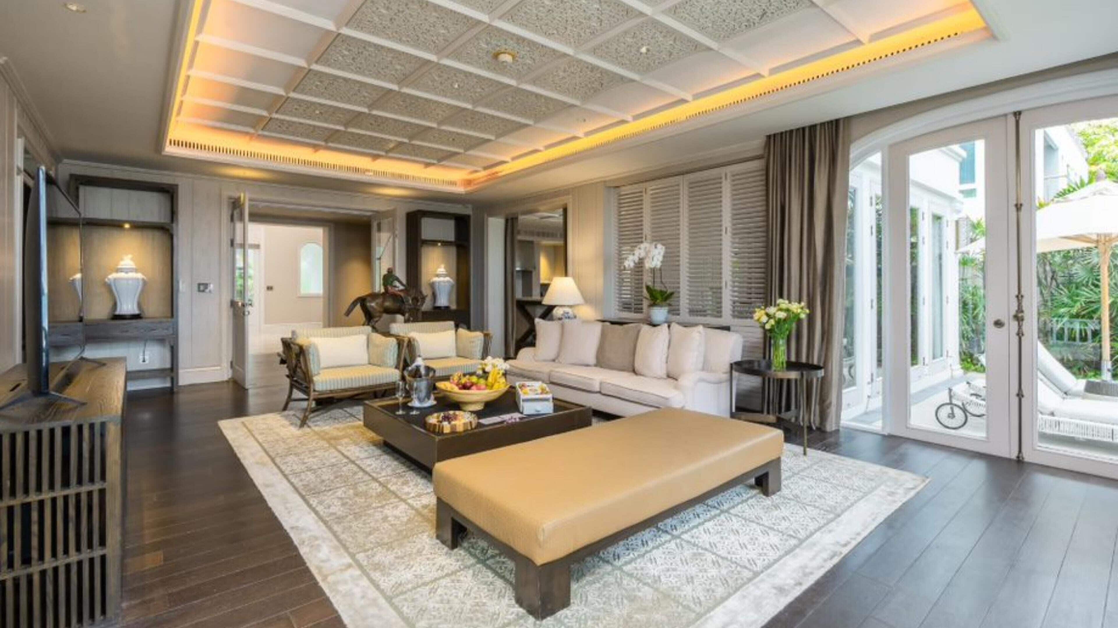 A spacious living area with a large sofa, a coffee table, and a bench. There is a fireplace, a dining area, and a view of the outdoors.