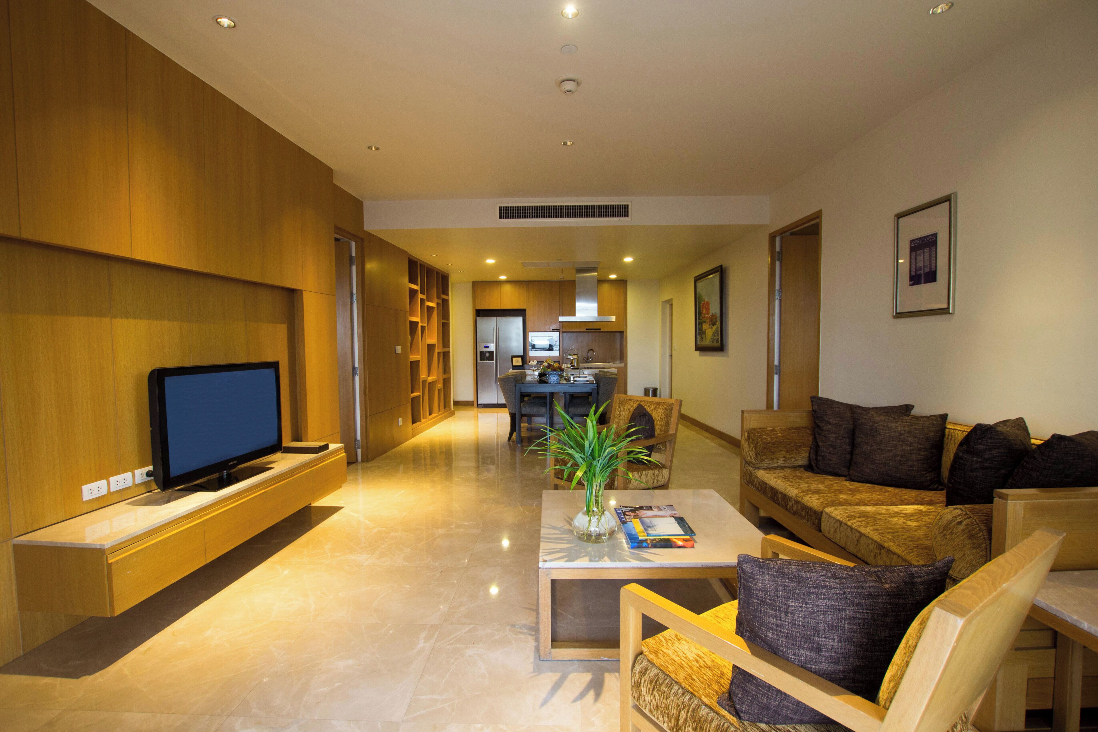 A modern living room with a flat-screen TV, a coffee table with a plant, a sofa, and a dining area in the background.