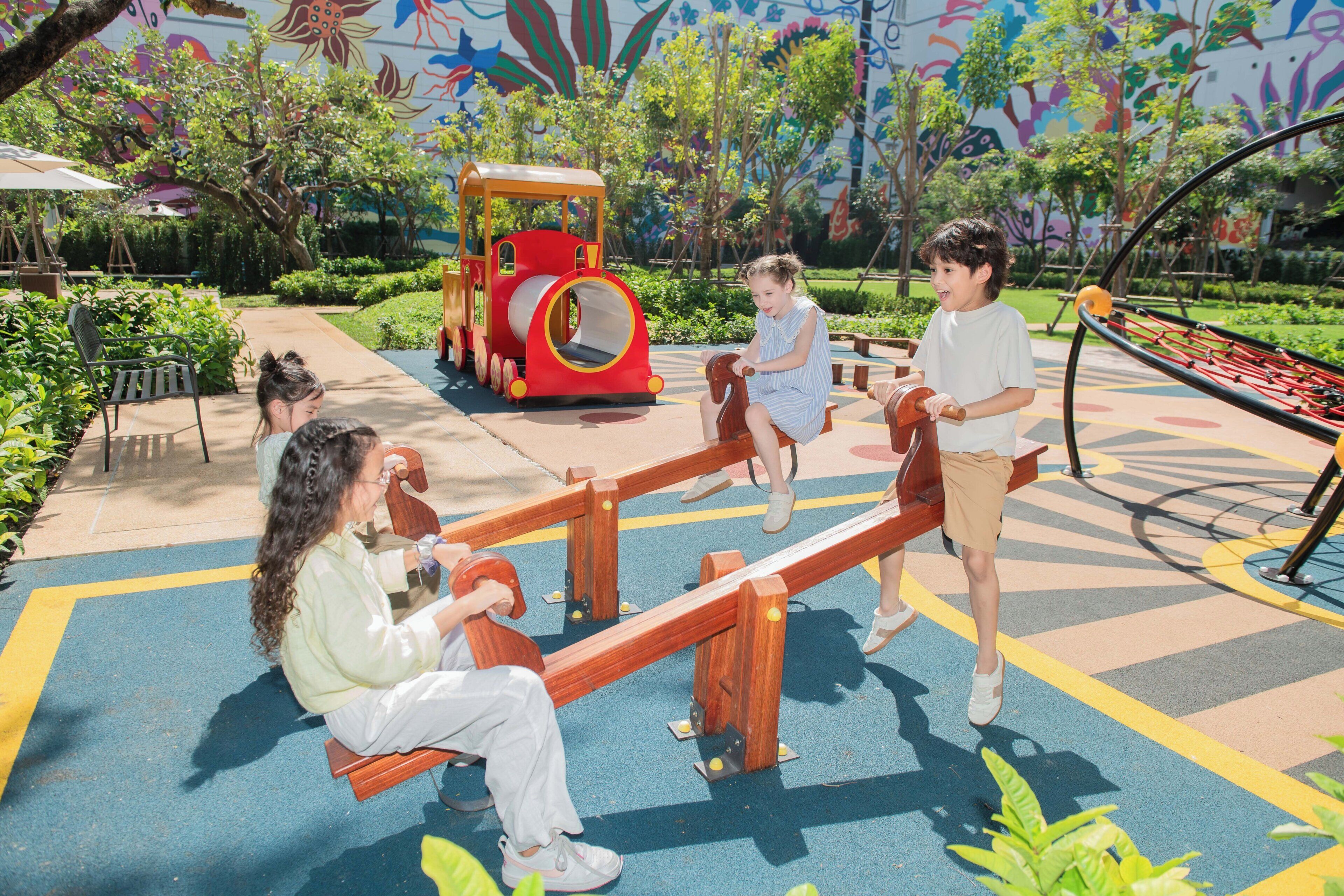 A playground with seesaws, a slide, and a colorful mural in the background.