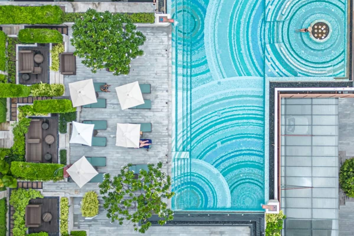 Vue aérienne d’un espace piscine sur le toit, avec un motif géométrique, entouré d’espaces aménagés pour s’asseoir et de verdure.