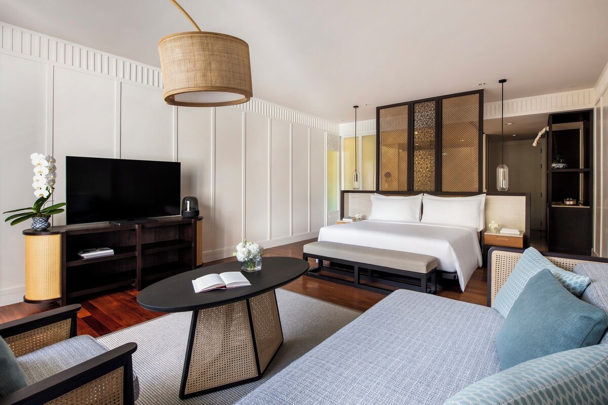 A modern hotel room with a large bed, a flat-screen TV, a dining table, and a sofa.