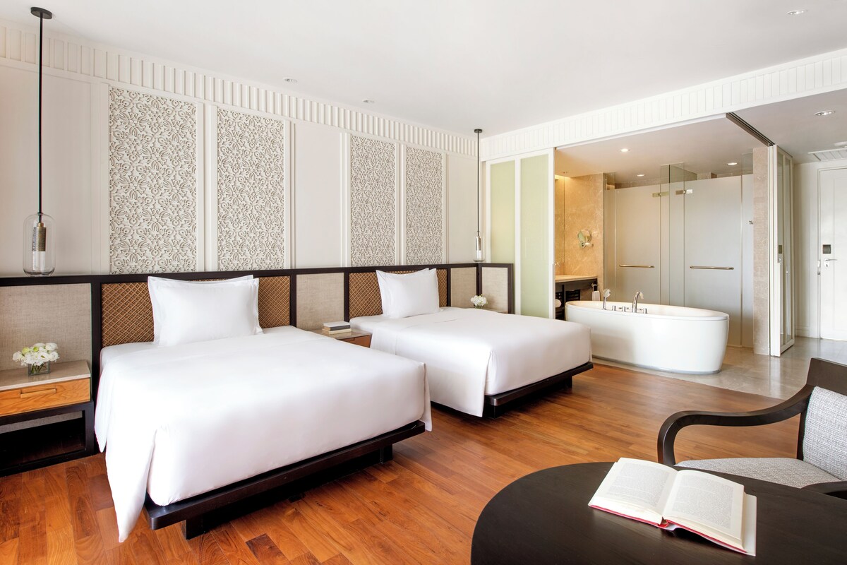 A hotel room with two beds, a sitting area with a table, and a separate bathroom with a bathtub.